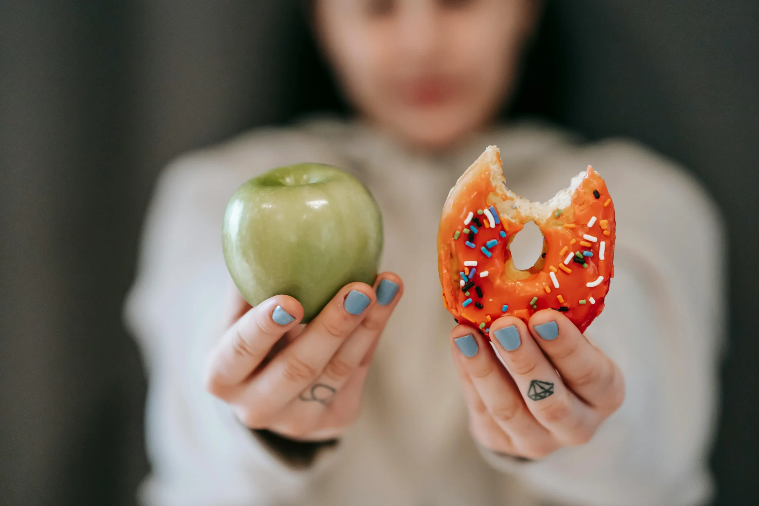 Uma mulher com uma maçã verde e uma rosquinha de doce nas mãos -alimentação